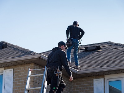two men climbing onto the roof of a house with a ladder