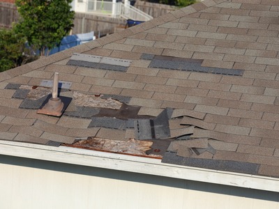 damage to a corner of a roof with shingles coming up